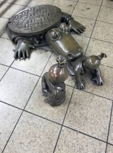 Rockefeller Park, New York, there is a monument/statue of a reptilian/croc with human hands wearing a suit and a baby with a money bag over his head and being dragged into an underground sewer/tunnel.